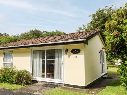 The exterior of a single-story house with sliding glass doors and a window surrounded by grass and bushes at Peacehaven Rosecraddoc Lodge near Liskeard