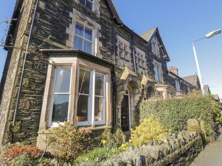 A stone terraced house with bay windows and an arched entrance surrounded by plants at 48 Oak Street in Windermere