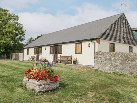 A single story building with a grey roof and flower pots next to the doors at Roan Cottage in Royal Wootton Bassett
