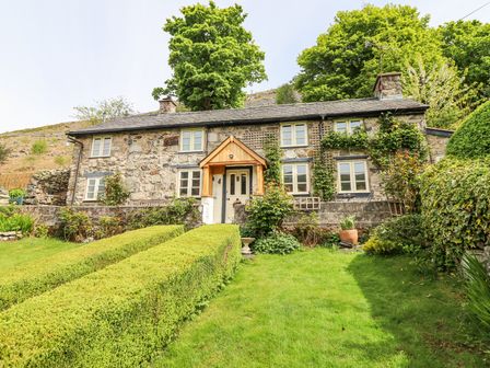 A stone cottage with green hedges and lawn in front surrounded by trees at Haulfryn in Llangynog