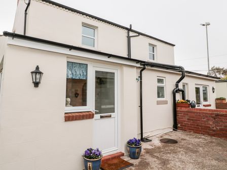 Exterior of a cream colored two story house with a white door two blue flower pots and a brick wall at St Cuthberts Cottage Beal near Holy Island