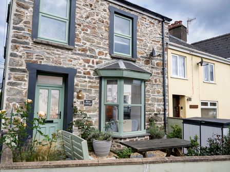 A stone house with green window frames and door with garden furniture and plants at Rose Cottage in St Dogmaels near Cardigan