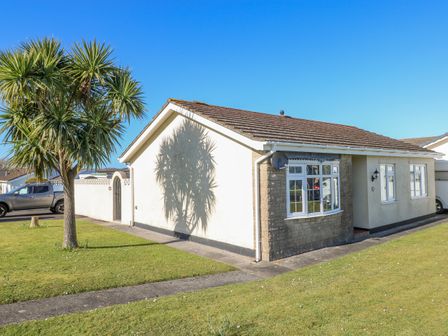 A single-story house with windows and a tree casting a shadow on the wall at Cann Ross in Penally near Tenby