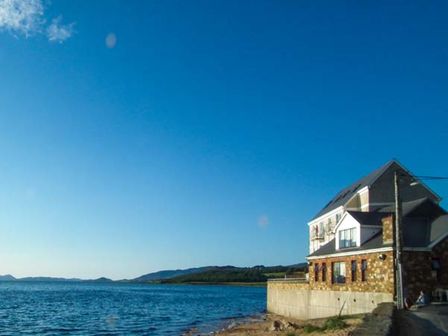 A building next to a body of water with hills in the background at The Beach House Apartment in Buncrana County Donegal