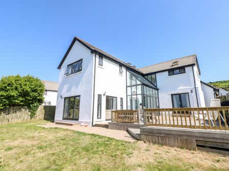 A two story white house with a wooden deck and glass wall extension in a garden at 1 Atlantic Haven in Llangennith