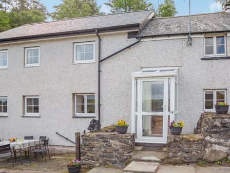 The exterior of a stone house with a white door porch and flower pots on stone walls at Bwthyn Fed'wr Gog in Maerdy near Bala