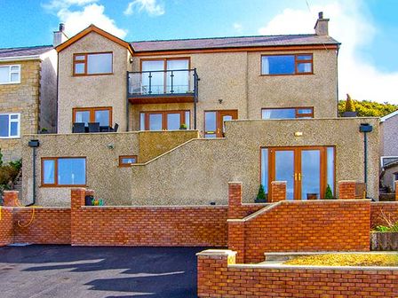 A two-story house with brown brick walls and multiple windows and doors in a residential area at Crud yr Awel in Y Felinheli near Caernarfon