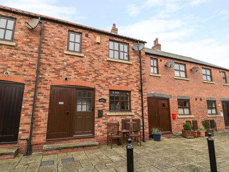 A brick exterior of a row of houses with brown doors and windows and outdoor chairs on the pavement at Little Venice in Whitby