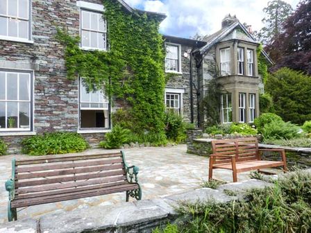 An outdoor patio with two wooden benches in front of a stone house covered with ivy at White Moss, Wood Close in Grasmere
