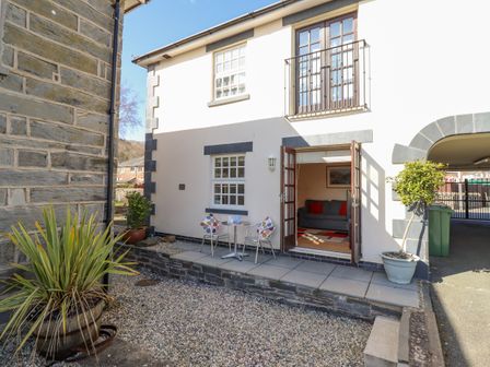 A small outdoor patio with two chairs and a table outside a house with open double doors at Taliesin in Porthmadog