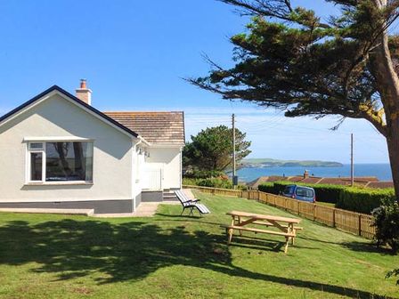 A white house with a lawn chairs and a picnic table in the garden near the sea at Quarterdeck in Bigbury-on-Sea near Modbury
