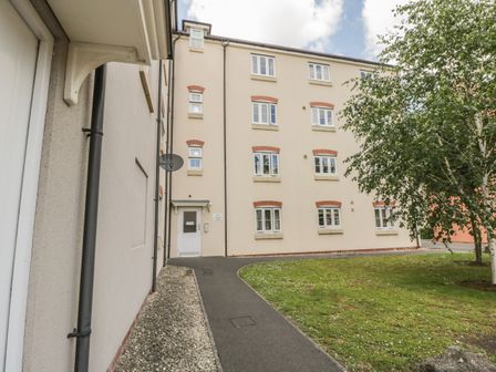 A pathway leading to the entrance of a multi-story residential building with windows and a tree on the grass at The Wesley Apartment in Wells