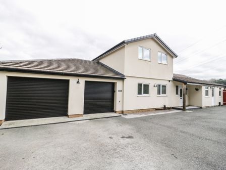The exterior of a two story house with two black garage doors and a driveway at Bryn Derw Holiday Cottage in Eglwysbach near Llanrwst and Conwy