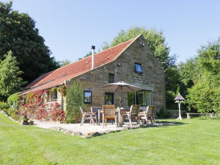 A stone house with a red tiled roof and outdoor wooden table and chairs under an umbrella at Dale View in Fryup near Lealholm