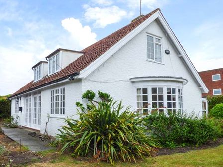 A white house with a brown tiled roof surrounded by plants and grass at The Dingle in Cromer