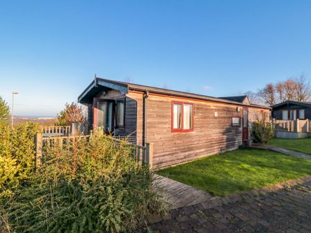 A wooden cabin with a small porch and grassy front yard at Hawthorne Lodge in Liverton near Danby