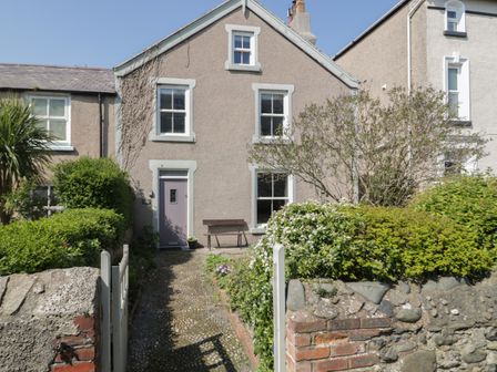 A stone pathway leading to a cottage entrance with a purple door surrounded by bushes and a stone wall at Trevor Cottage in Llandudno
