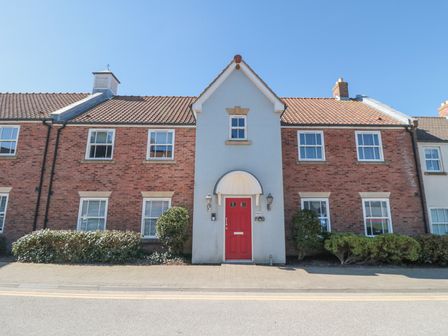 A brick townhouse with a red front door and small bushes along the front at Sunny Bay in The Bay near Filey