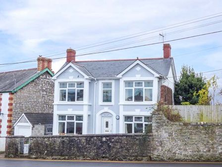 A two-story detached house with white framed windows and a stone wall in front at Pen Hill in Llantwit Major
