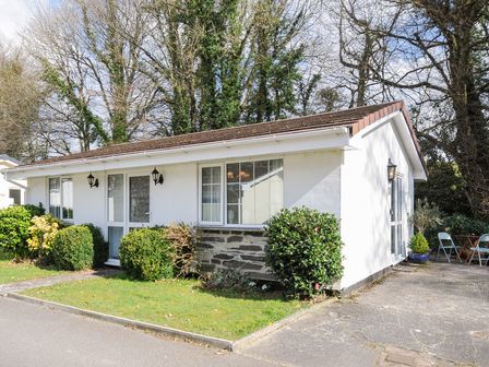 A single-story white house with shrubbery in front and folding chairs on the side at No 1 The Heathers Rosecraddoc Lodge near Liskeard