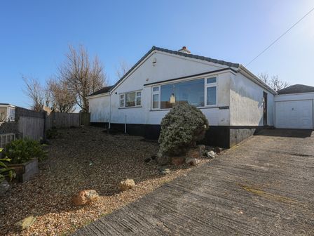 A single-story white house with a gravel yard and a driveway leading to a garage at Tegfan in Trearddur Bay