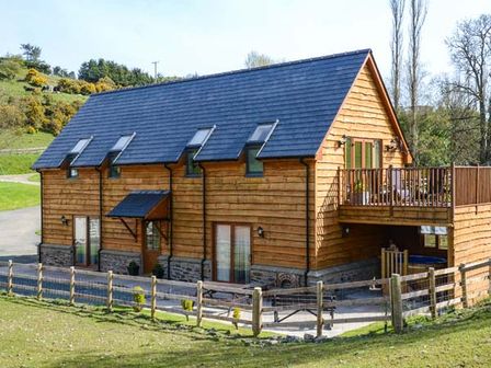 A wooden house with a fenced yard and a balcony at Brynhir Farm in Howey near Llandrindod Wells