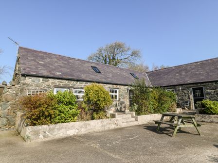 Stone cottages with shrubbery and a wooden picnic table in the yard at Bwthyn yr Helyg in Pwllheli