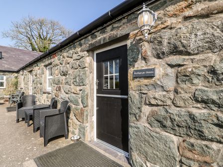The outside of a stone building with a black door and outdoor chairs at Bwthyn yr Onnen (Ash Cottage) in Pwllheli