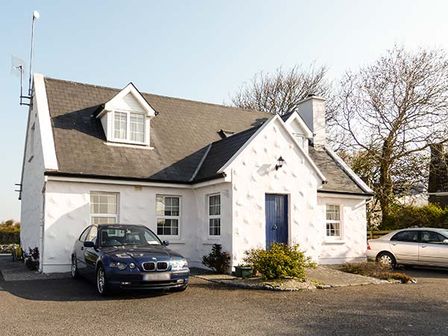 A white house with a blue door and two parked cars outside at Brandy Harbour Cottage in Ballinderreen near Kinvara County Galway