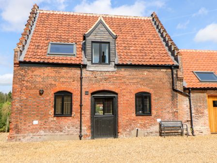 A red brick house with a black door two black windows a bench and a tiled roof at Tricker's Cottage in Morton on the Hill near Lenwade