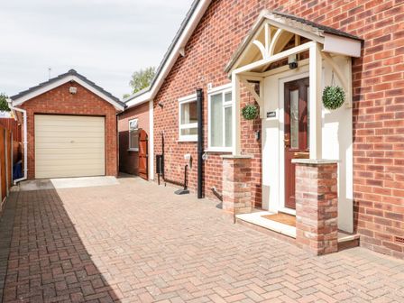 A brick driveway leading to a garage and a porch entrance with two hanging plants at Cwtch Cottage in Deganwy near Llandudno