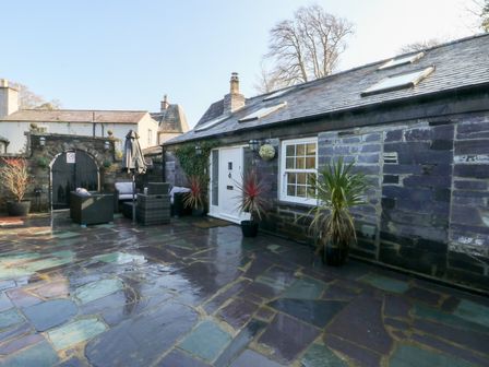 A patio with stone flooring plants outdoor seating and an arched gate at Bryn Derwen Coach House in Bethesda