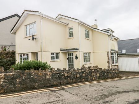 A two story cream house with multiple windows and a stone wall in front at The Old Bakehouse in Llantwit Major