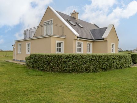 A beige two-story house with a hedge and grassy yard at 8 Lios Na Sioga in Binghamstown near Belmullet County Mayo