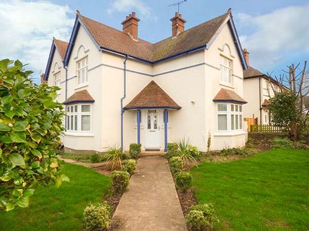 A two-story house with tiled roof white exterior and a walkway with bushes leading to the front door at Lily House in Minehead