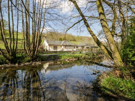 A house with a stone garage by a river and trees at Riverside Torver near Coniston