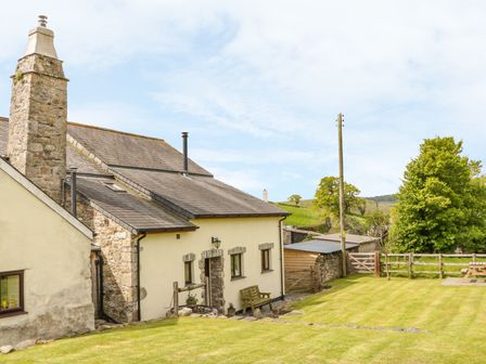 A stone and plaster house with a chimney and a small lawn with bench and wooden fencing at Higher Whiddon Farm Whiddon Well Ashburton near Newton Abbot