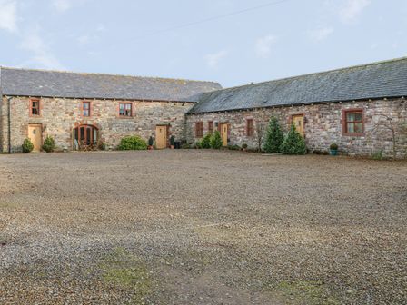 A stone building with multiple wooden doors and windows with a gravel courtyard in front at Swift Cottage in Milton near Brampton