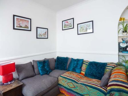 A corner of a living room with a gray and patterned sofa with blue cushions and framed pictures on white walls at Tidewood Polzeath