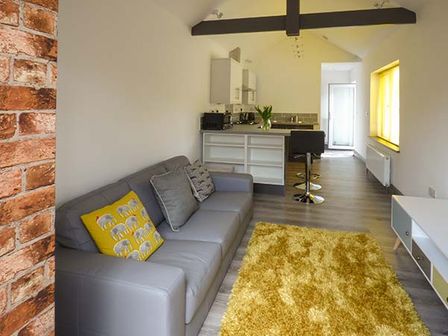 A living room with a gray sofa and yellow rug next to a kitchen with bar stools at White Cottage Annexe in Tenby