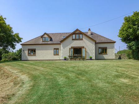 A white house with brown window frames and a garden with a picnic table at Fferam Y Llyn in Rhosgoch near Cemaes Bay