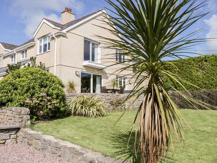 A garden with a palm tree and shrubs outside a two storey house at Bryn y Don in Benllech