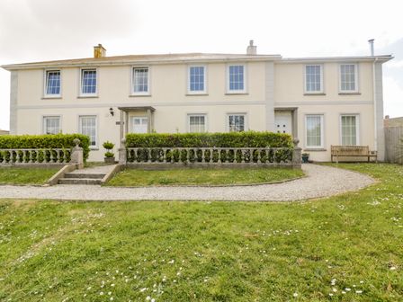 A two story house with multiple windows hedges and a stone pathway with a bench on the side at Tremanners St Agnes