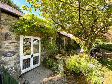 Stone cottage entrance with white doors and greenery a tree and outdoor seating at Hendy Cottage Sardis near Criccieth