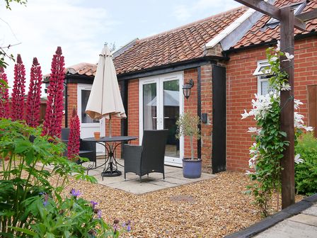 An outdoor patio area with a table umbrella chairs red and white flowers and a potted plant at Jack's Corner in King's Lynn