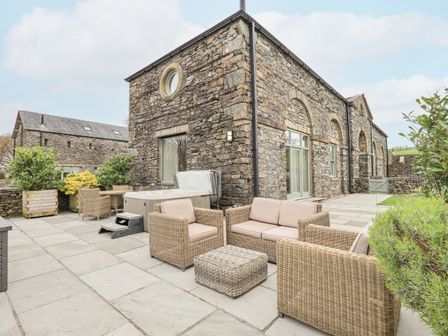 An outdoor patio area with stone walls wicker seating plants and a hot tub at Hazel Cottage in Backbarrow near Newby Bridge