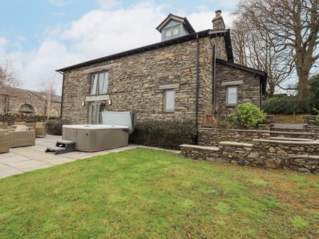 A stone exterior house with a patio hot tub and outdoor seating area at Keepers Cottage in Backbarrow near Newby Bridge