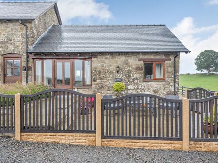 A stone building with a slate roof behind a black metal fence at The Granary in Llanfair Caereinion near Welshpool