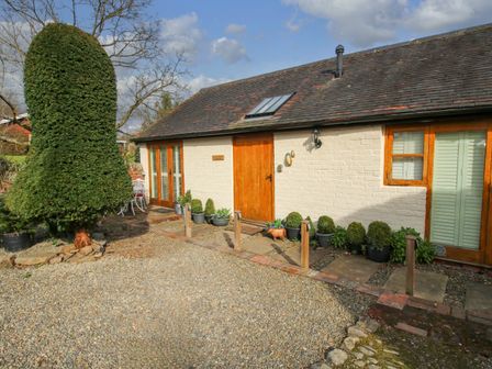The exterior of a single-story building with wooden doors windows with shutters potted plants and a gravel driveway at The Milking Parlour in Yarpole near Leominster