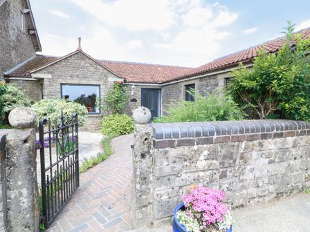 A stone house with a tiled roof a black metal gate a brick pathway and plants and flowers at Leigh Holt in Waterlip near Shepton Mallet